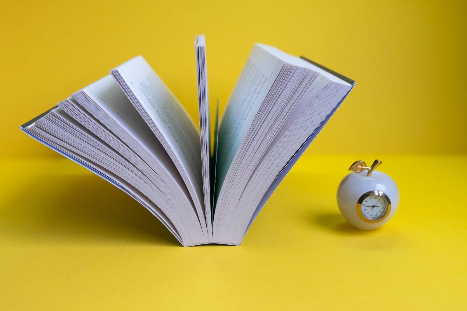 Open book with an apple and a clock — education still-life